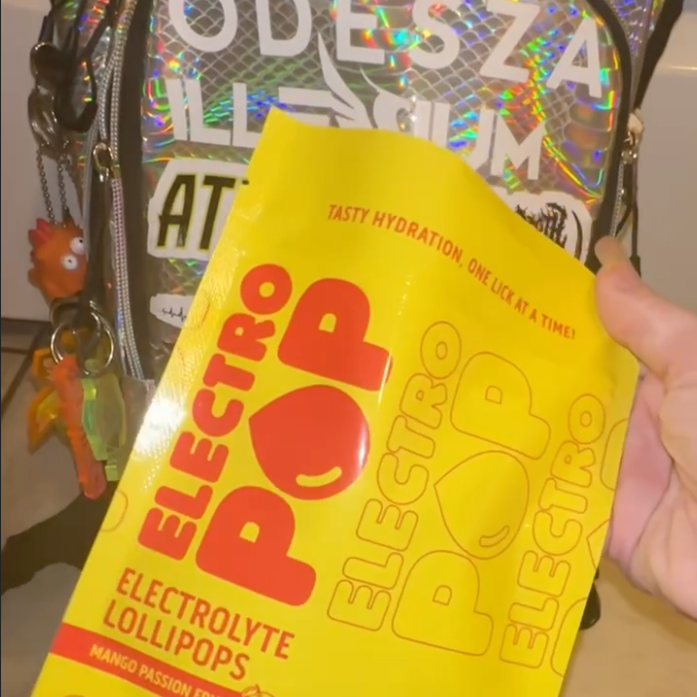 Yellow Electro Pop lollipop package held in front of a backpack.